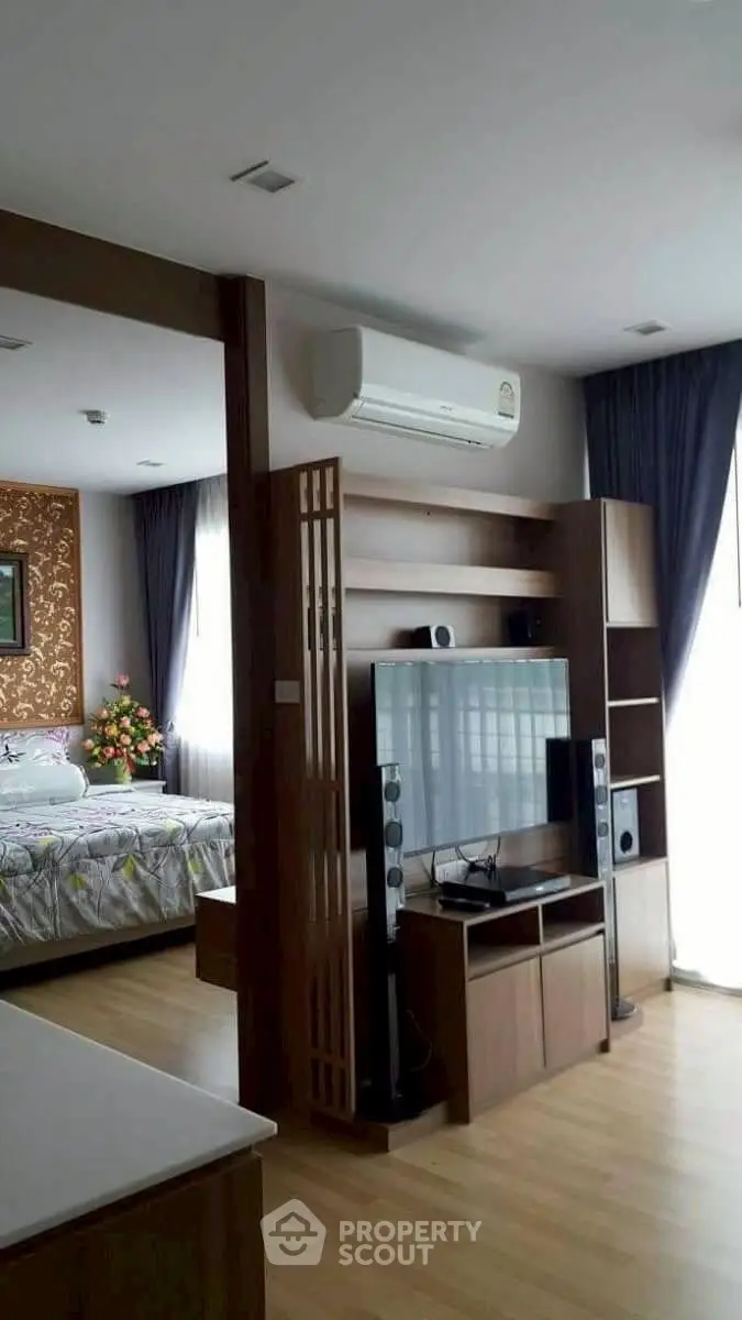 Modern open-plan living room with TV and air conditioning, adjacent to a cozy bedroom.