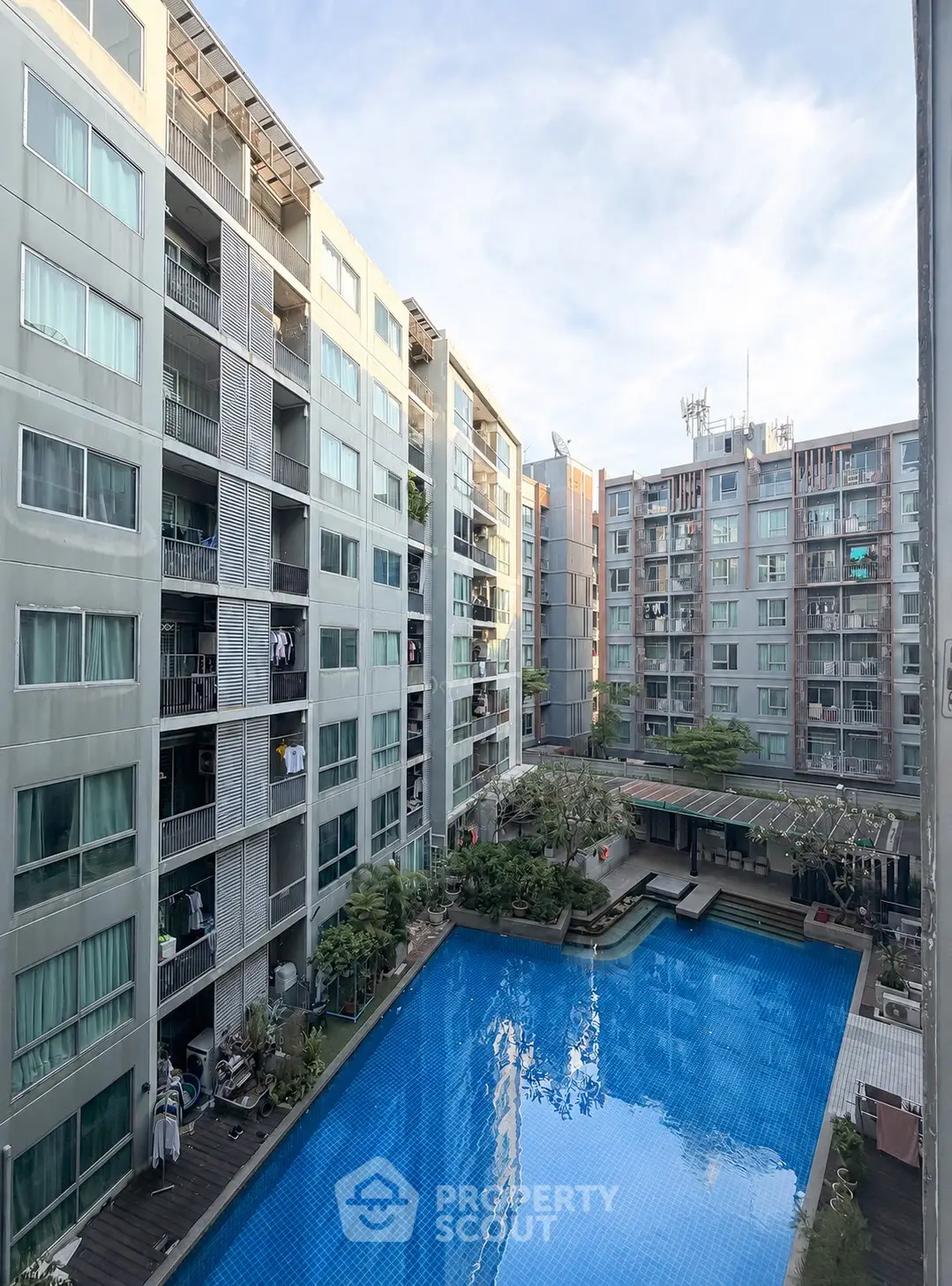 Modern apartment complex with a large swimming pool and lush greenery, offering a serene urban living experience.