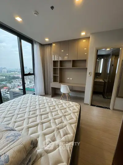 Modern bedroom with city view, featuring built-in desk and large windows for natural light.