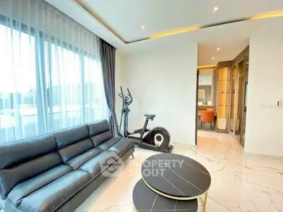 Modern living room with sleek black sofa and exercise bike, featuring elegant marble flooring and large windows.