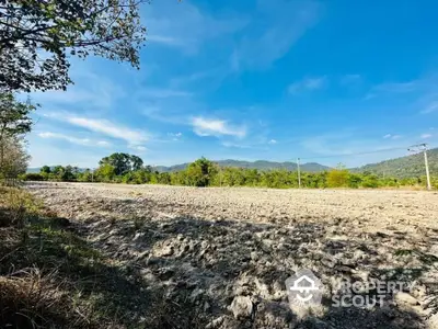 Expansive vacant land ready for development, boasting fertile soil and a picturesque backdrop of lush mountains under a clear blue sky.