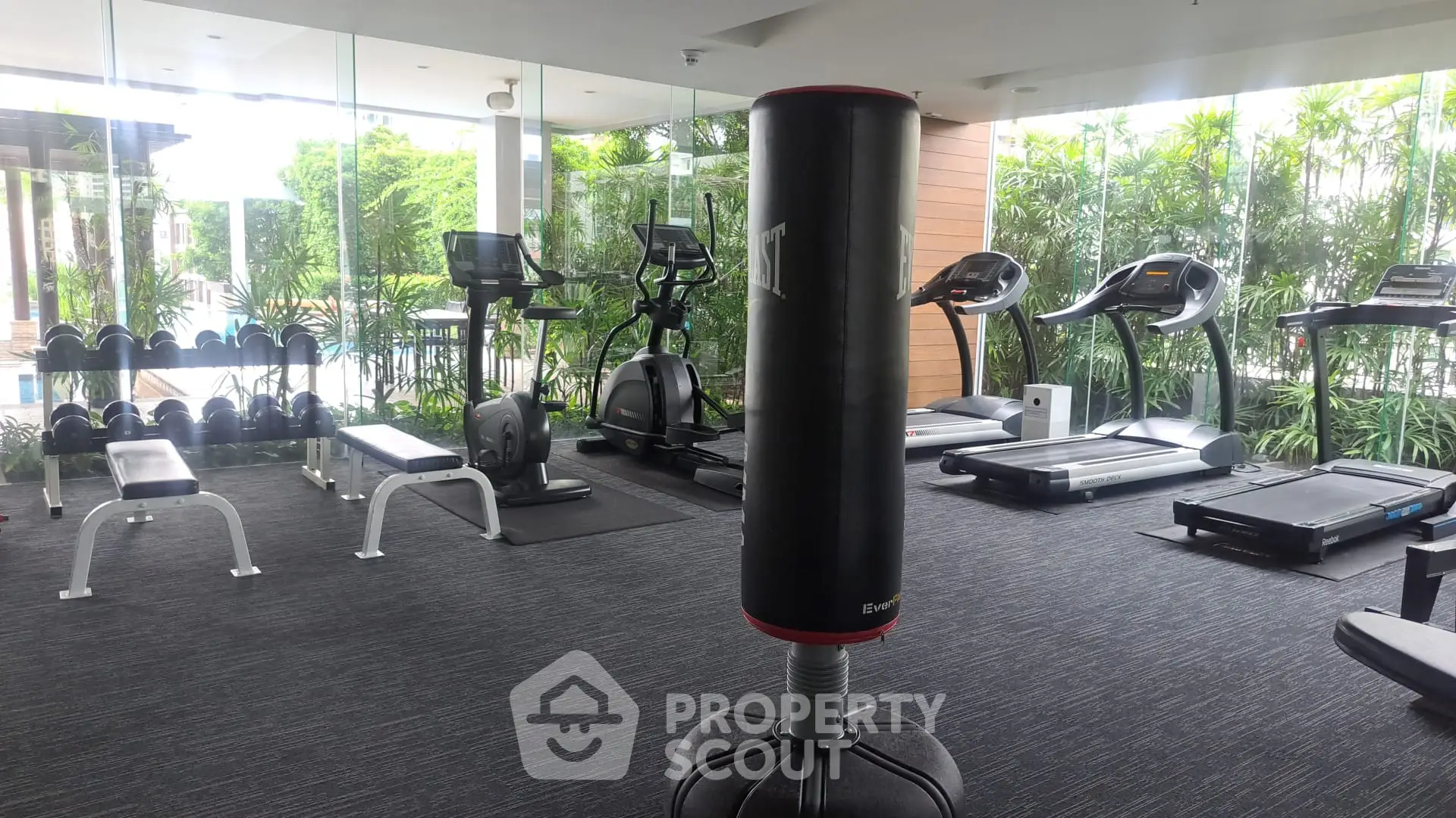 Modern gym with state-of-the-art equipment and lush garden views, perfect for fitness enthusiasts.