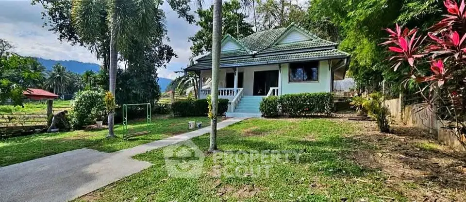 Charming countryside house with lush garden and scenic mountain backdrop.
