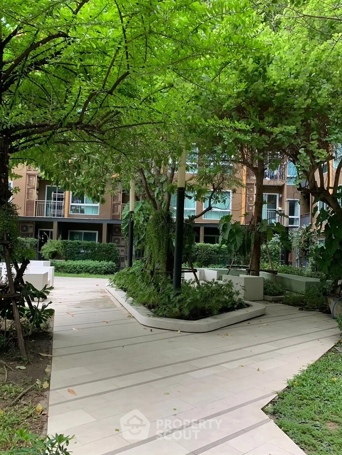 Lush garden pathway in modern residential complex with green foliage and stylish architecture.