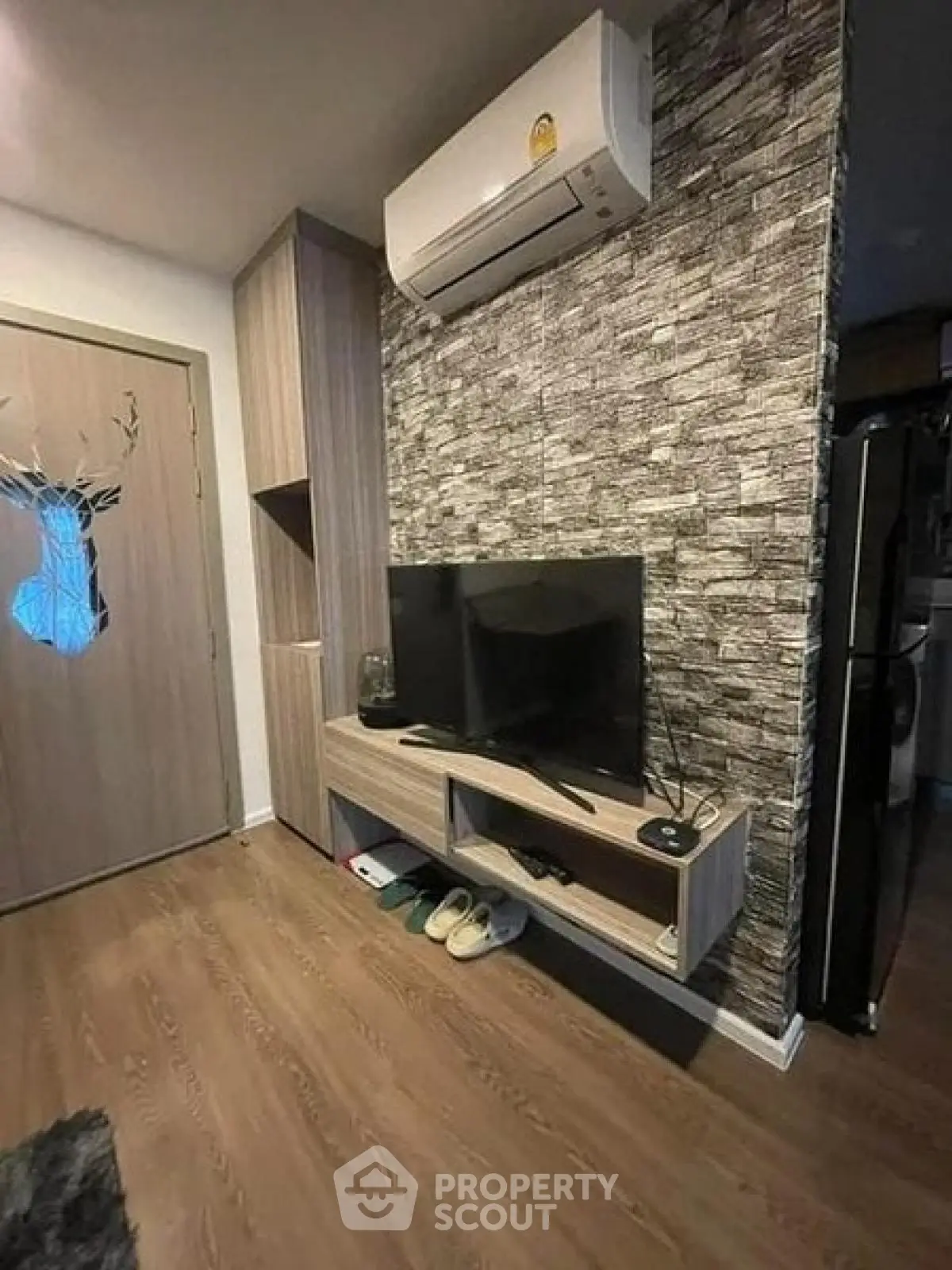 Modern living room with stylish TV setup and air conditioning, featuring wood flooring and textured wall design.