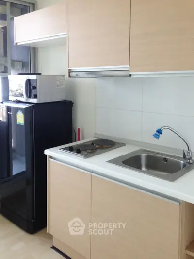 Modern kitchen with sleek cabinets, compact fridge, and electric stove in a cozy apartment.