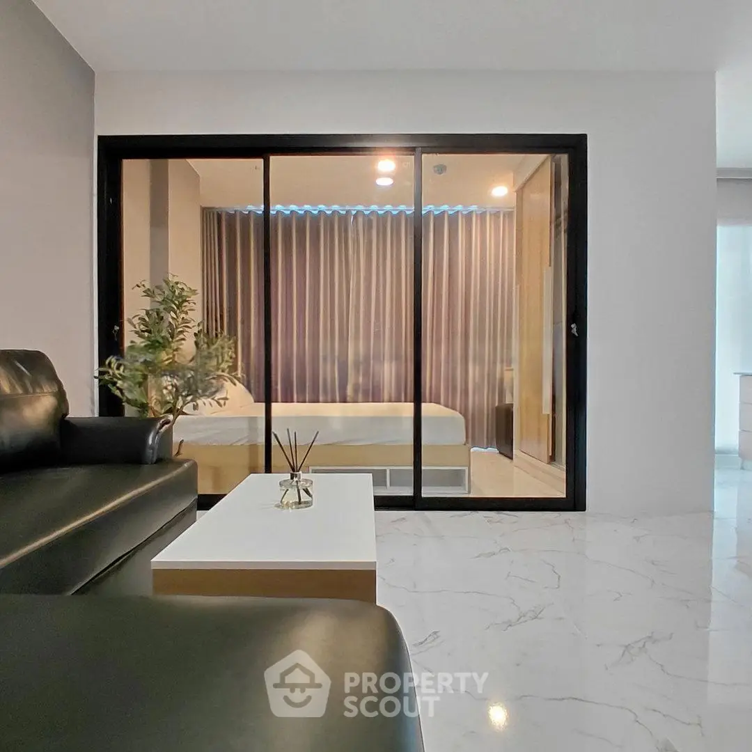 Modern living room with sleek design and glass partition leading to a cozy bedroom.