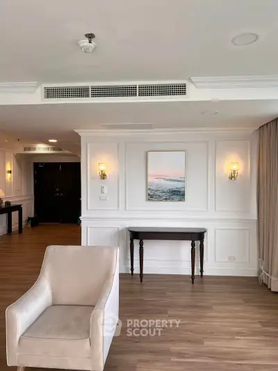 Elegant living room with classic decor and wooden flooring, featuring a cozy armchair and wall art.