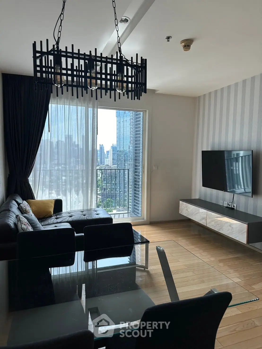 Modern living room with city view, stylish chandelier, and sleek furniture.