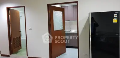 Modern apartment interior with kitchen and bathroom doors, featuring a sleek refrigerator.