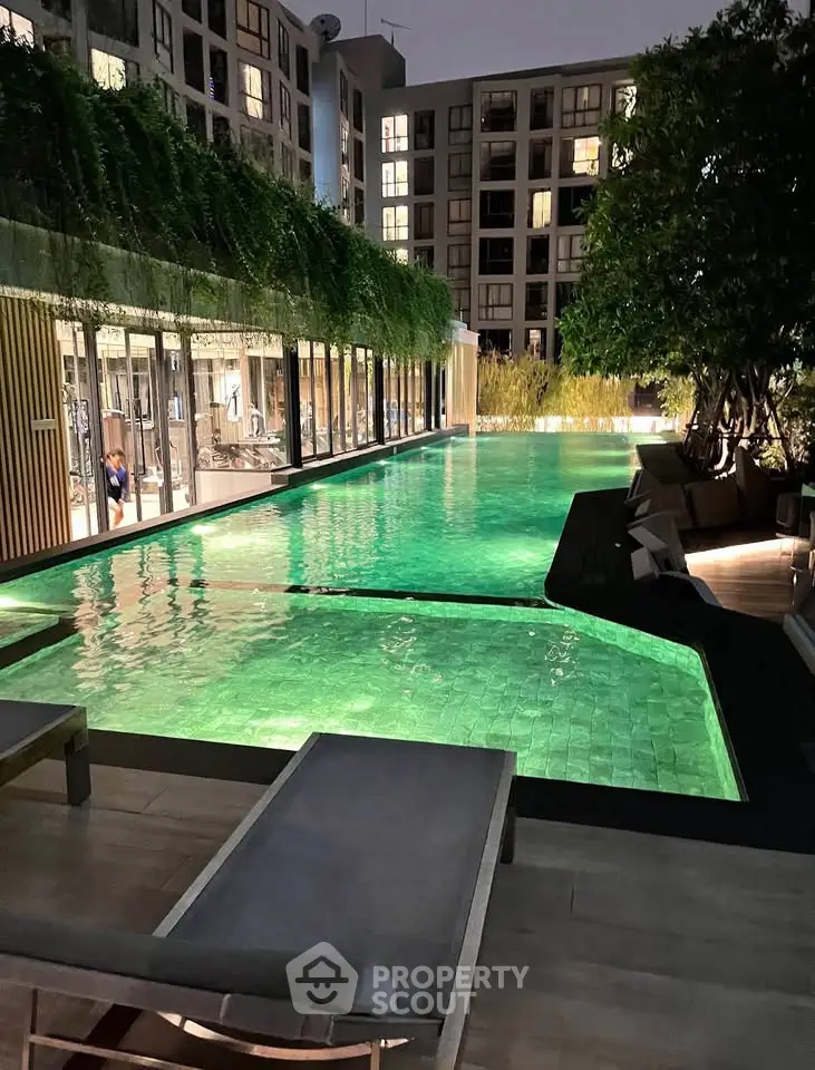 Luxurious apartment complex with illuminated swimming pool and lush greenery at night.
