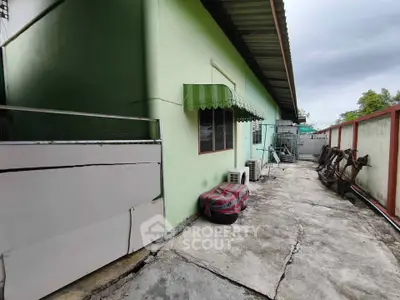 Spacious outdoor area with potential for renovation, featuring a green building exterior and ample concrete space.