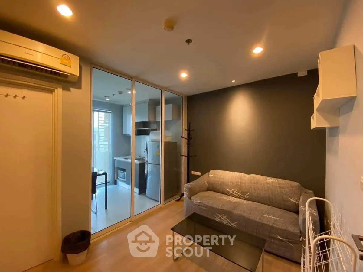 Modern living room with glass partition and kitchen view, featuring cozy sofa and sleek design.