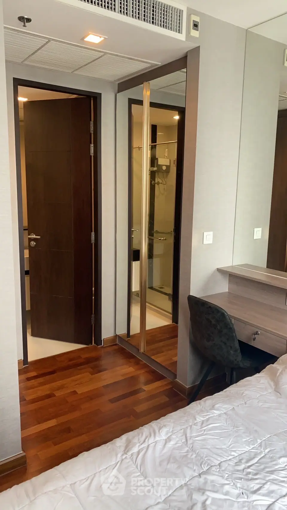 Modern bedroom with wooden flooring, mirrored closet, and ensuite bathroom in a stylish apartment.