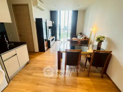 Modern living room with open kitchen and city view, featuring sleek furniture and wooden flooring.