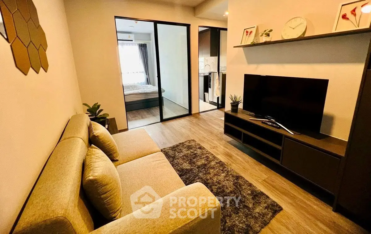 Modern living room with cozy sofa and TV, open view to bedroom