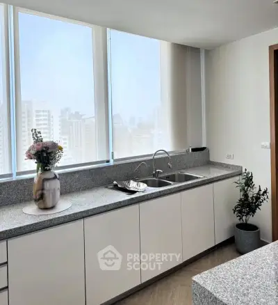 Modern kitchen with large windows and sleek countertops in a high-rise apartment.