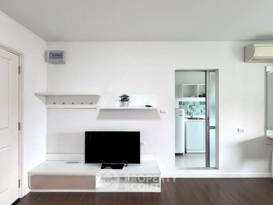 Modern living room with sleek TV stand and glimpse of kitchen featuring washing machine