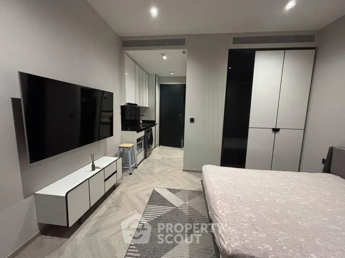 Modern bedroom with sleek TV setup and compact kitchen area in stylish apartment.