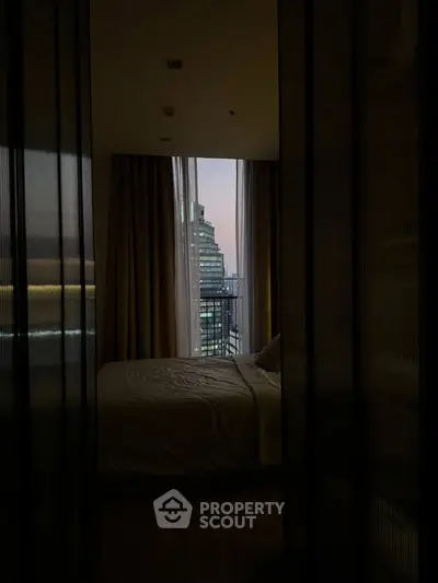 Cozy bedroom with city view through large window at dusk