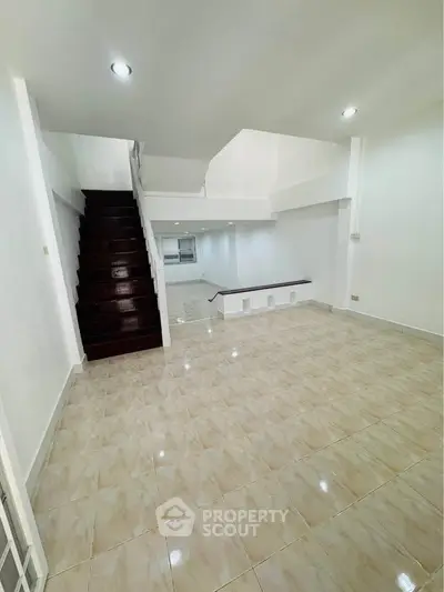 Spacious modern living room with elegant staircase and glossy tiled flooring.