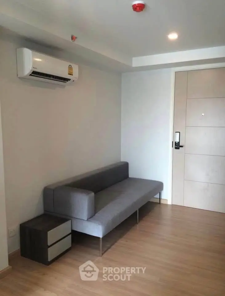 Modern minimalist living room with sleek gray sofa and air conditioning unit.