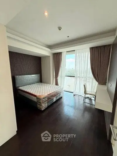 Spacious bedroom with large window and modern furnishings in a high-rise apartment.