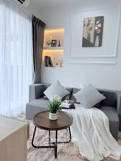 Chic modern living room with cozy gray sofa, stylish decor, and natural light from large window.