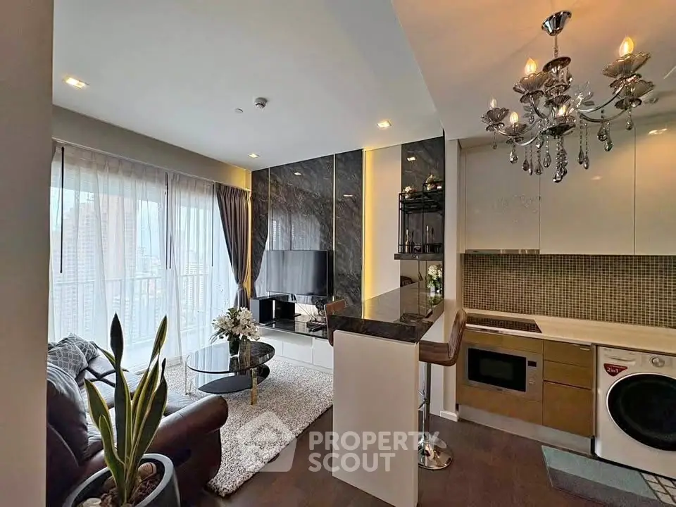 Luxurious modern living room with open kitchen, featuring elegant chandelier and large windows.