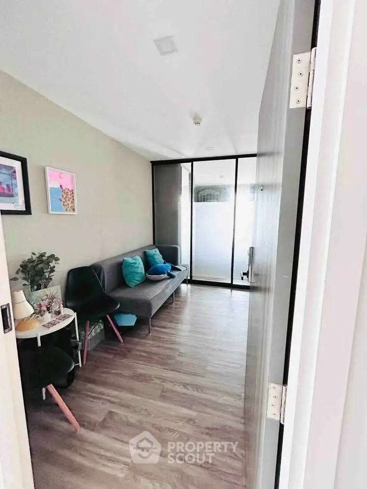 Modern living room with stylish decor and glass partition, featuring cozy seating and wooden flooring.