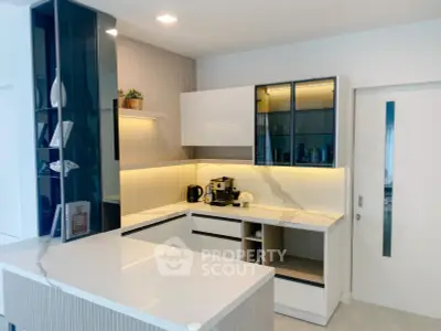 Modern kitchen with sleek white cabinets and marble countertops, featuring a coffee machine and stylish decor.