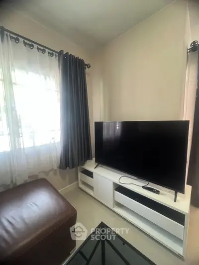 Cozy living room with modern TV setup and stylish curtains, perfect for relaxation.