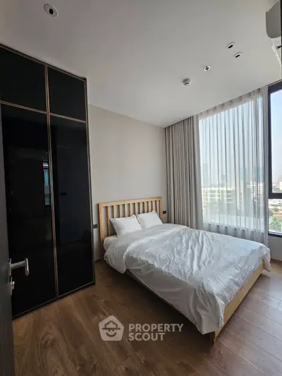 Modern bedroom with large window and wooden flooring in a high-rise apartment.