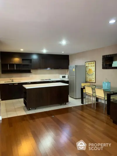 Spacious modern kitchen with island and dining area, featuring sleek dark cabinetry and hardwood floors.