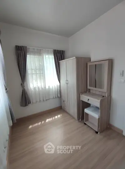 Bright bedroom with wooden wardrobe and dressing table, featuring large windows and elegant curtains.
