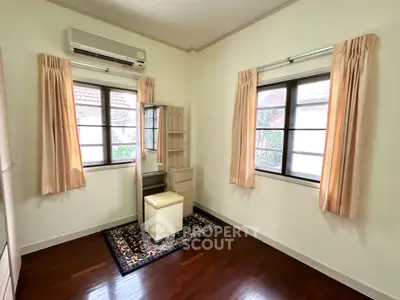 Cozy and well-lit bedroom with polished wooden flooring, air conditioning, and large windows draped with elegant curtains.