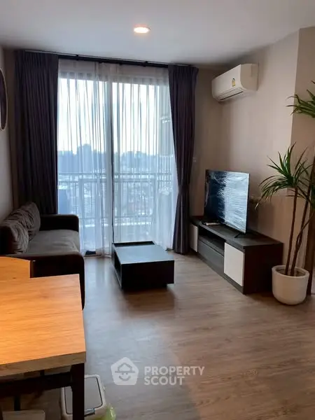 Modern living room with large window and city view, featuring a cozy sofa and sleek TV setup.