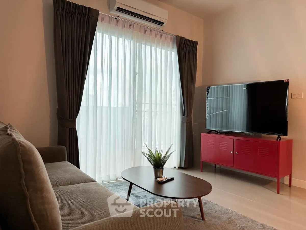 Modern living room with stylish furniture and large TV, featuring natural light from a window with elegant curtains.