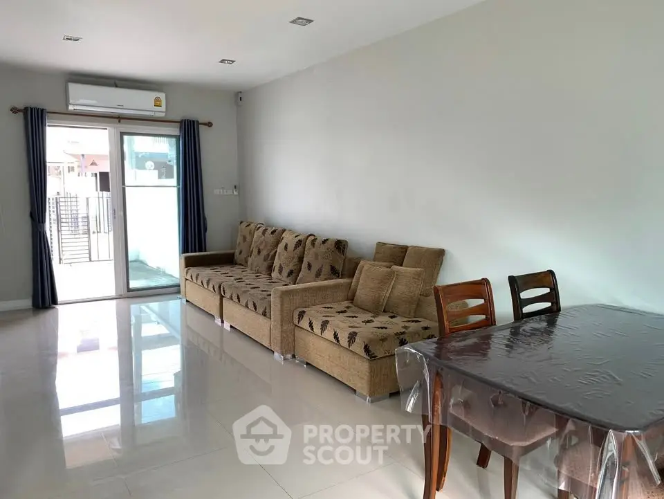 Spacious living room with modern sofa and dining area, featuring large windows for natural light.