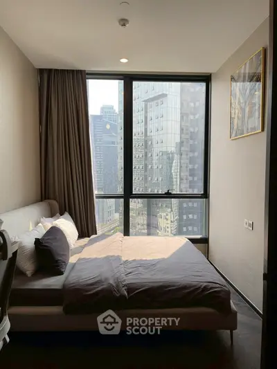 Modern bedroom with city view and large window, featuring stylish decor and natural light.