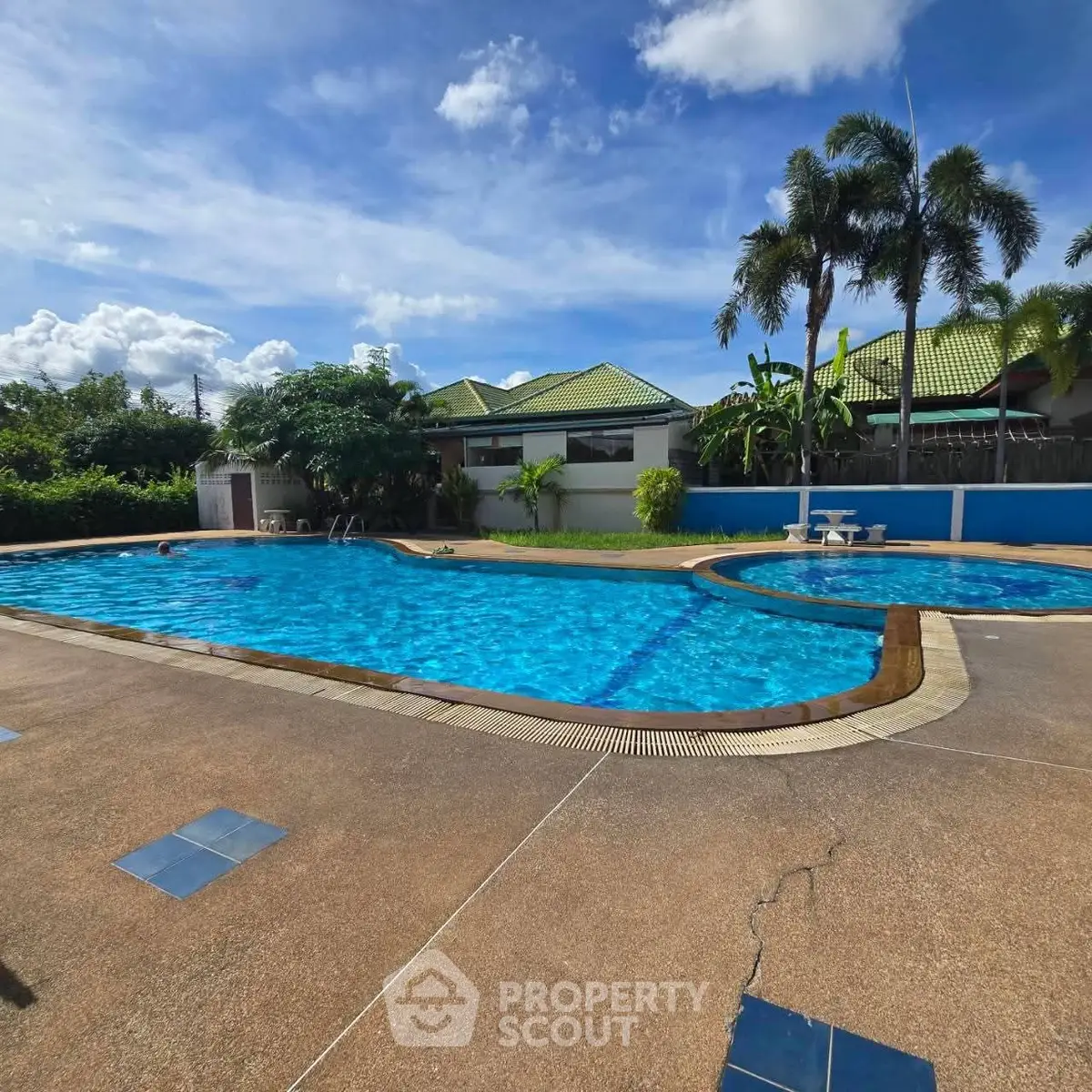 Stunning outdoor pool area with lush greenery and clear blue skies, perfect for relaxation and leisure.