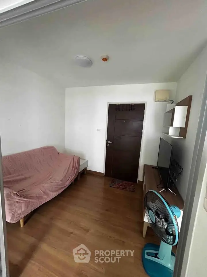 Cozy living room with wooden flooring, sofa, TV, and fan, perfect for relaxation.