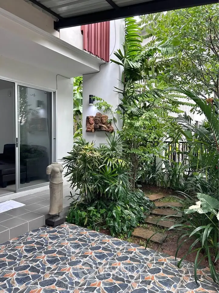 Charming garden entrance with lush greenery and artistic decor in modern home.