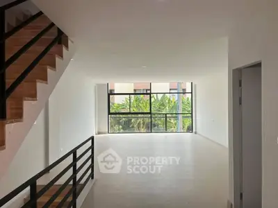 Spacious modern living room with large windows and staircase, offering abundant natural light and garden view.