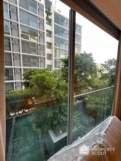 Modern apartment view with lush greenery and pool from large window.