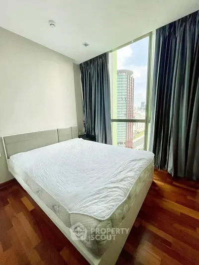 Modern bedroom with large window offering city view and wooden flooring.