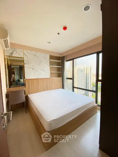 Modern bedroom with large windows offering city views, featuring a stylish bed and elegant decor.