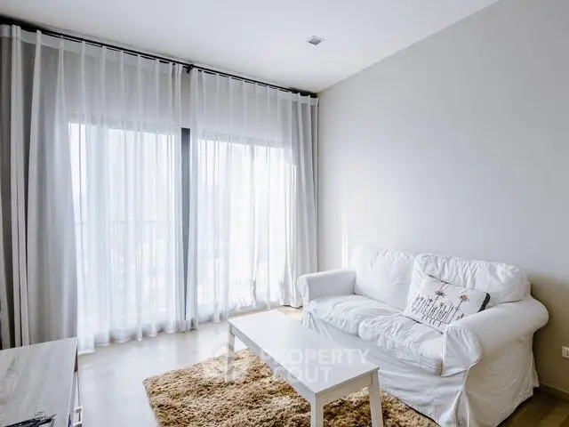 Bright and cozy living room with white sofa and sheer curtains, perfect for relaxation.