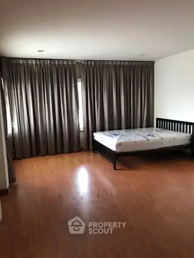 Spacious bedroom with wooden flooring and large windows for natural light.