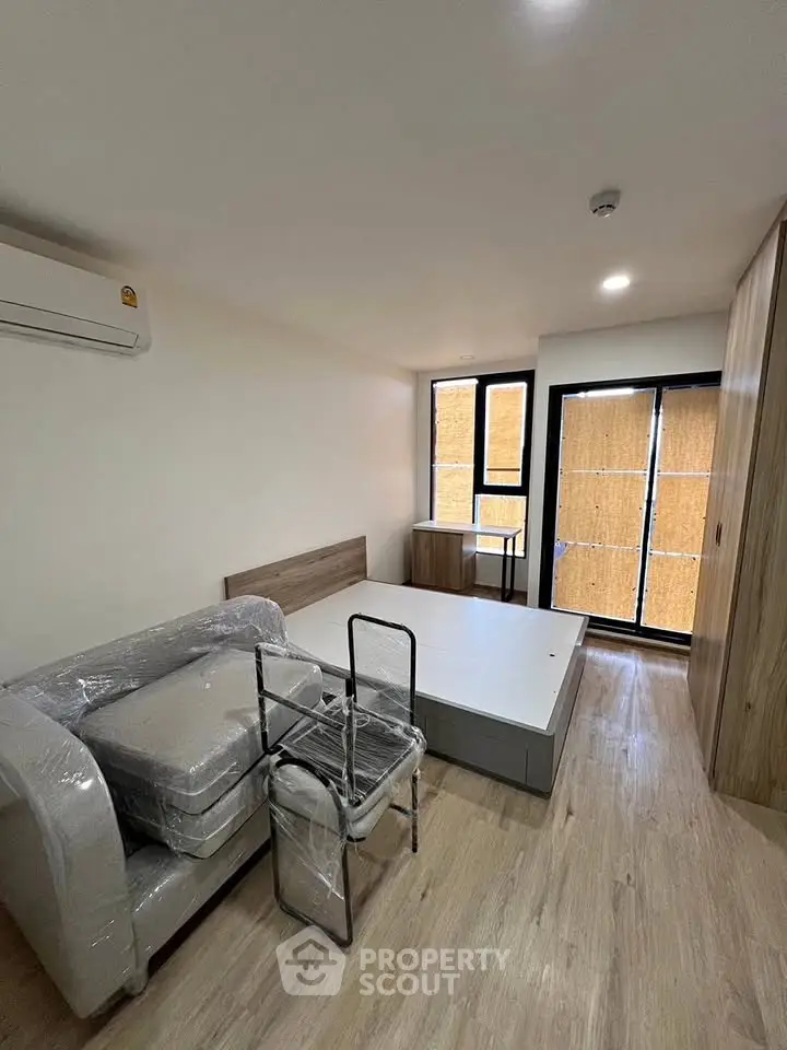 Modern bedroom with minimalist design and natural light, featuring a bed, sofa, and air conditioning.